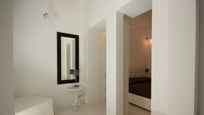 Un dormitorio moderno con una cama grande, una mesita de noche pequeña, un espejo y una pared blanca.