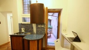 Una cocina compacta con un lavamanos, una estufa y un ordenador portátil sobre una mesita.
