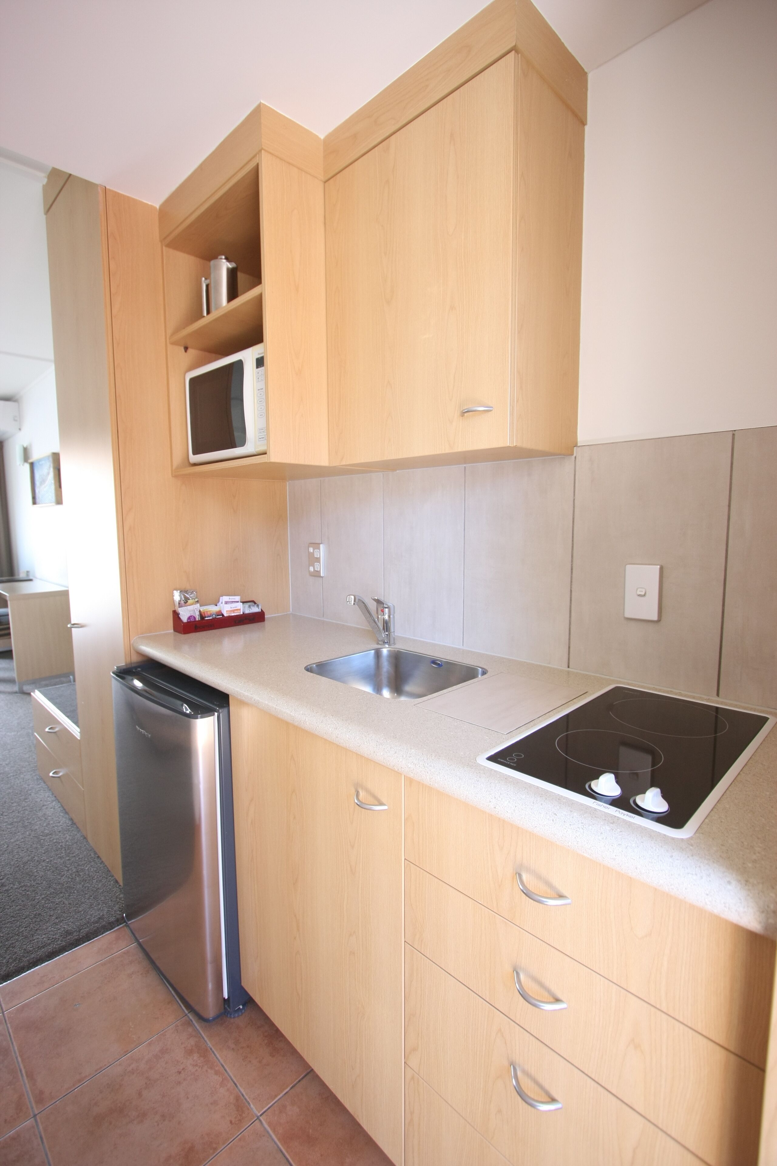 A compact kitchen with wooden cabinets, a stainless steel sink, and a built-in microwave.