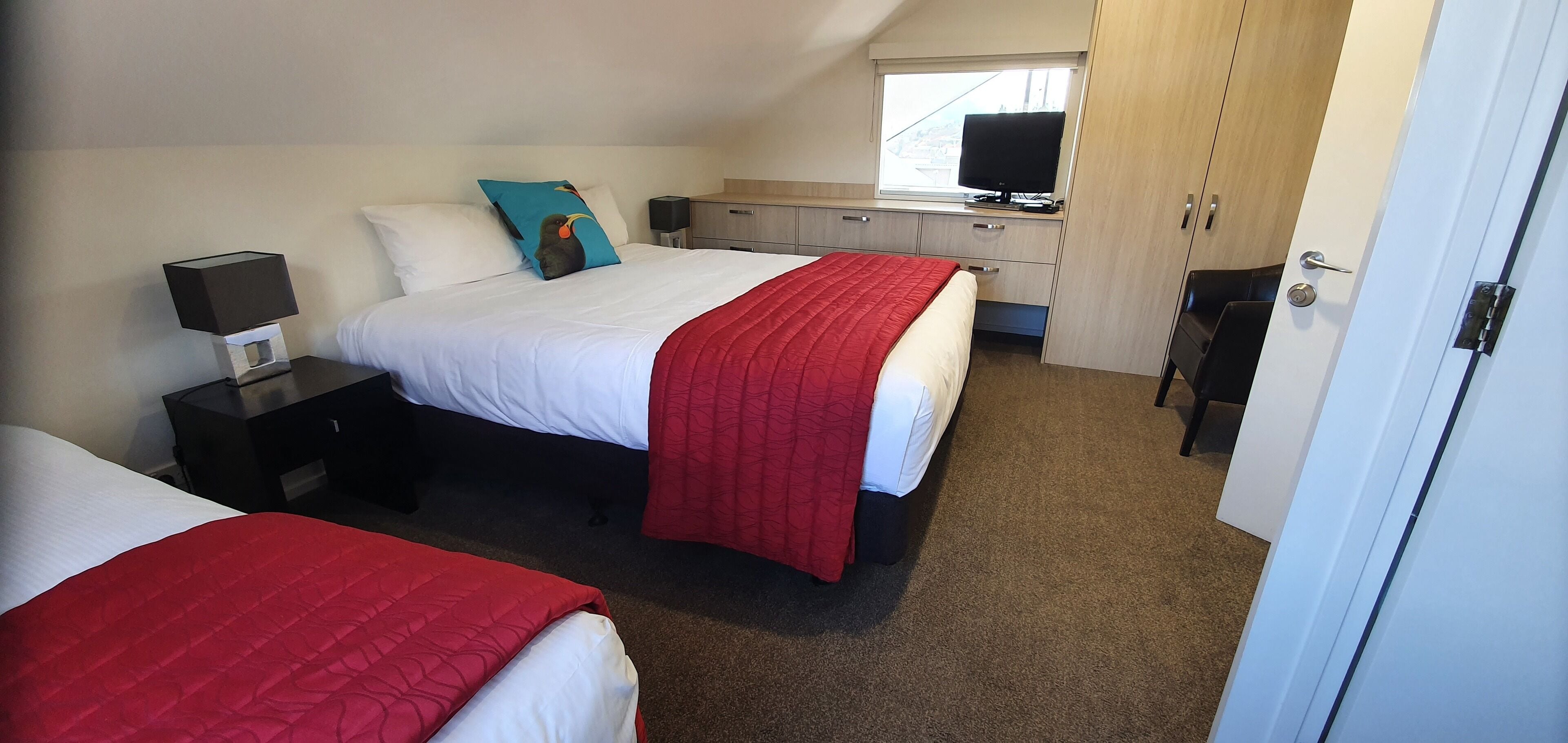 A hotel room with two beds, a desk with a computer, a TV, and a wardrobe.