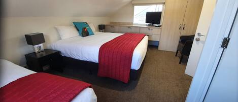A hotel room with two beds, a desk with a computer, a TV, and a wardrobe.