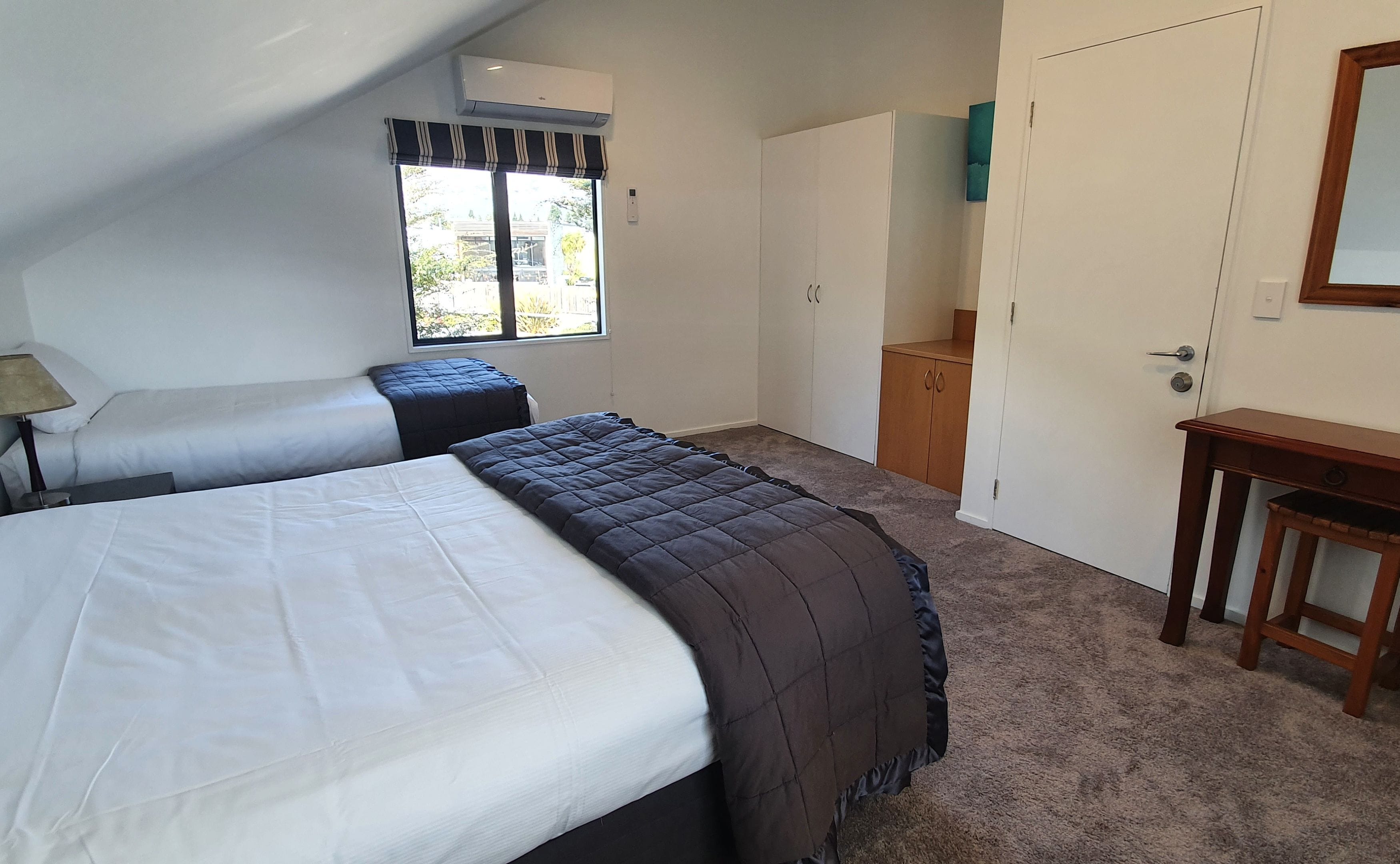 A bedroom with two beds, a window with a view, a wardrobe, and a small table.