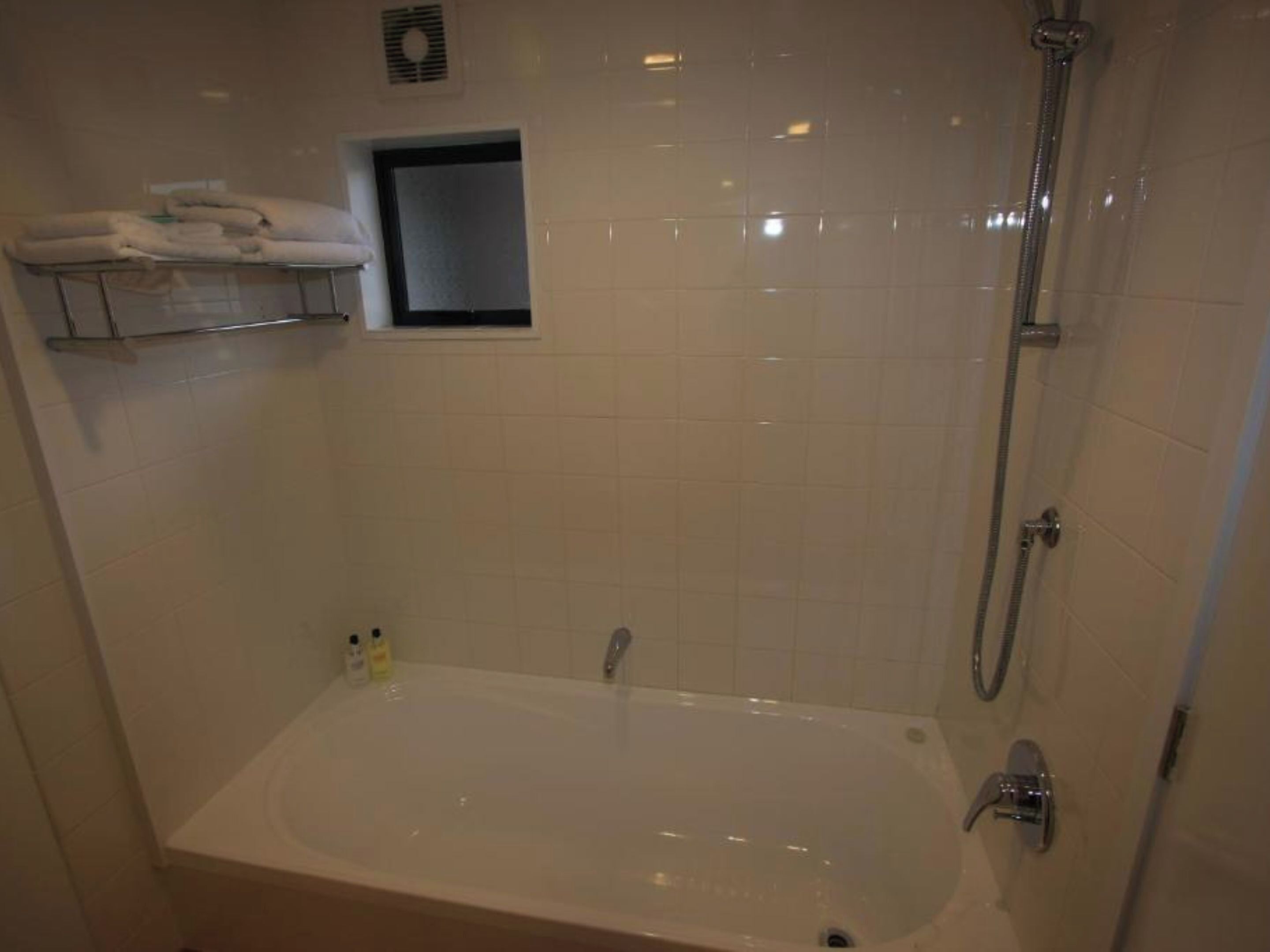 Un baño con bañera, ducha y un estante pequeño con toallas.