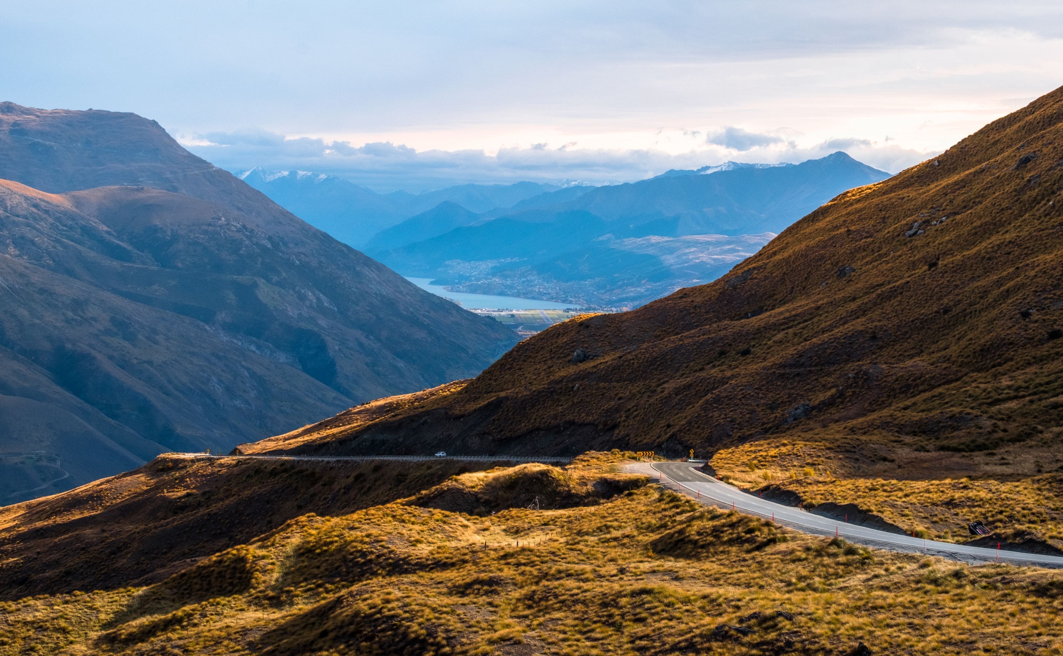 A mountain road with a guardrail, surrounded by rugged terrain and distant mountains.