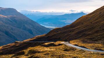 A mountain road with a guardrail, surrounded by rugged terrain and distant mountains.
