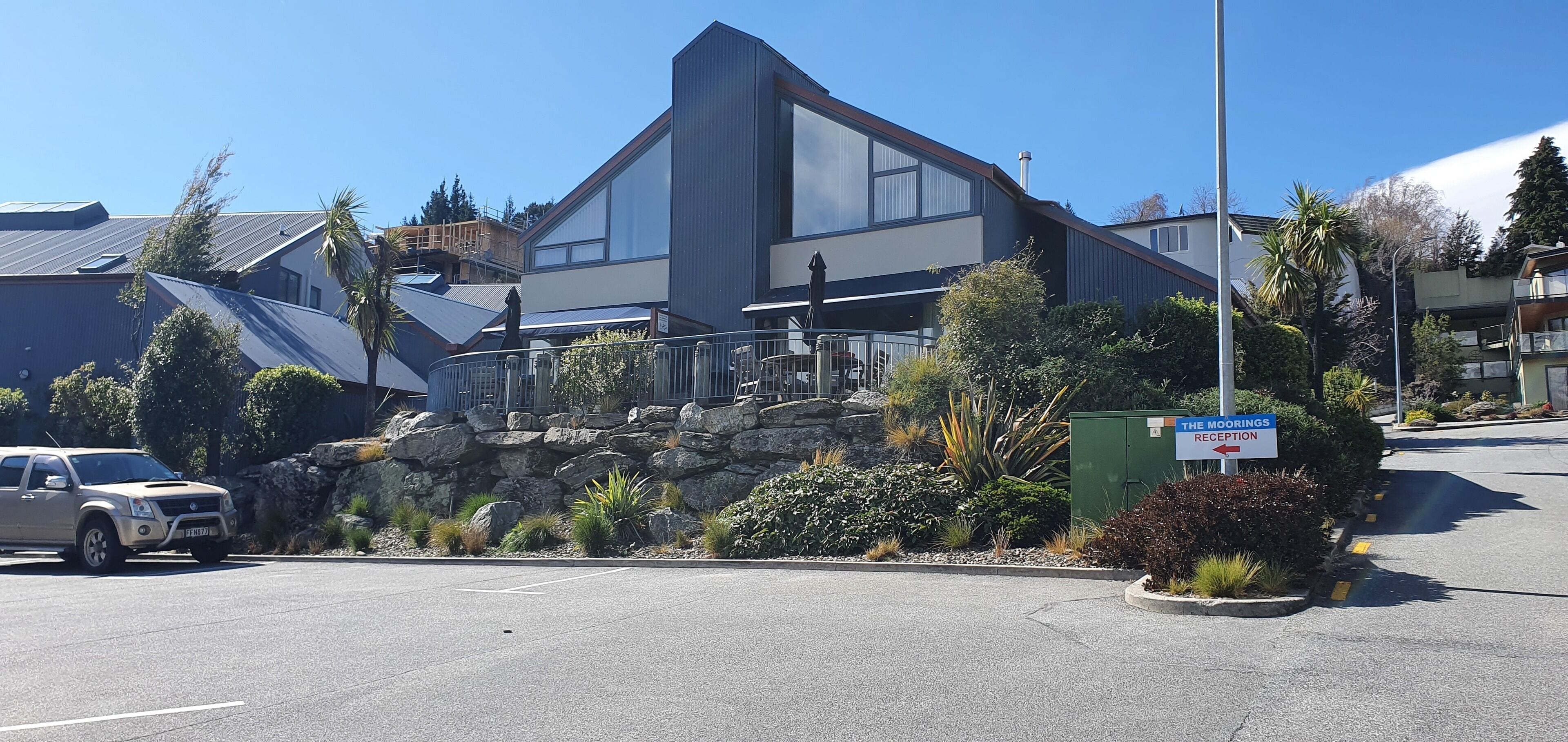 A modern building with a large glass facade, a stone retaining wall, and a sign indicating a reception area.