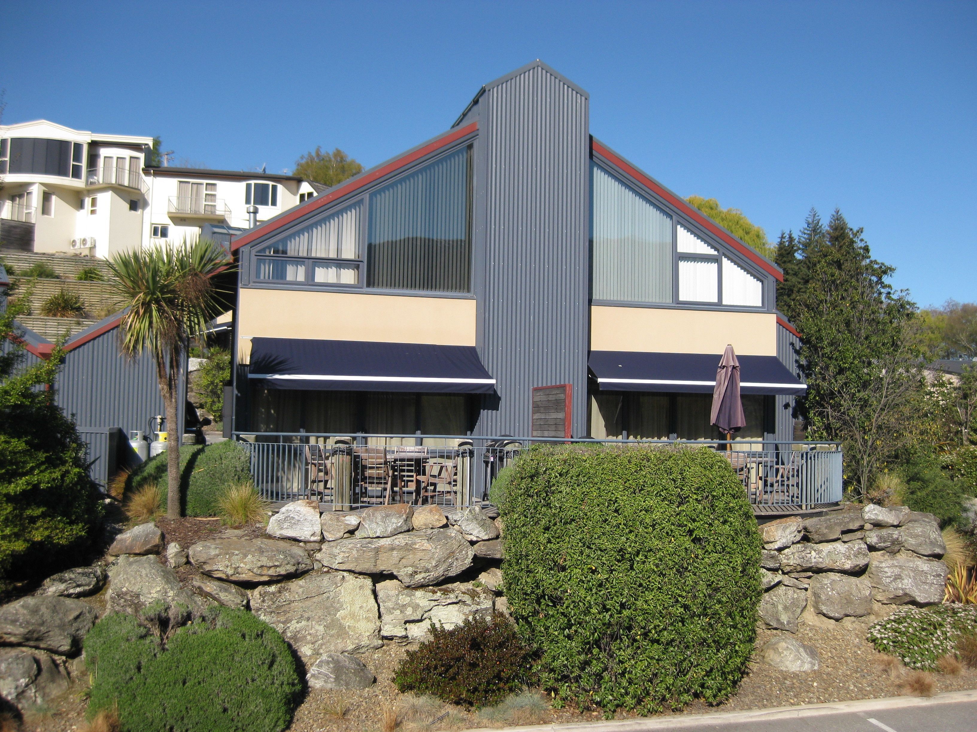 A modern two-story building with a stone foundation, large windows, and a balcony with outdoor seating.