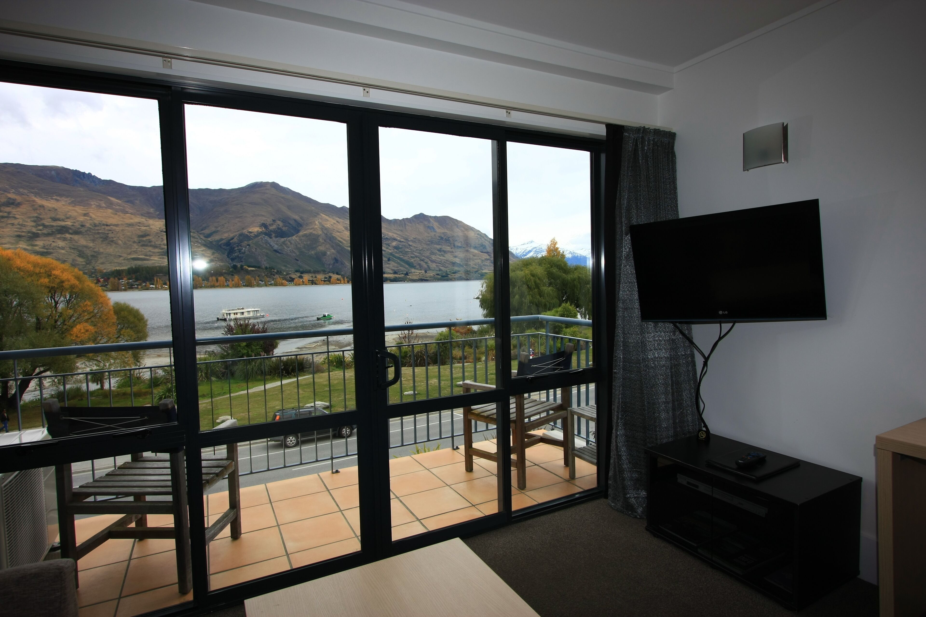 A room with a large sliding glass door leading to a balcony with a view of a lake and mountains.