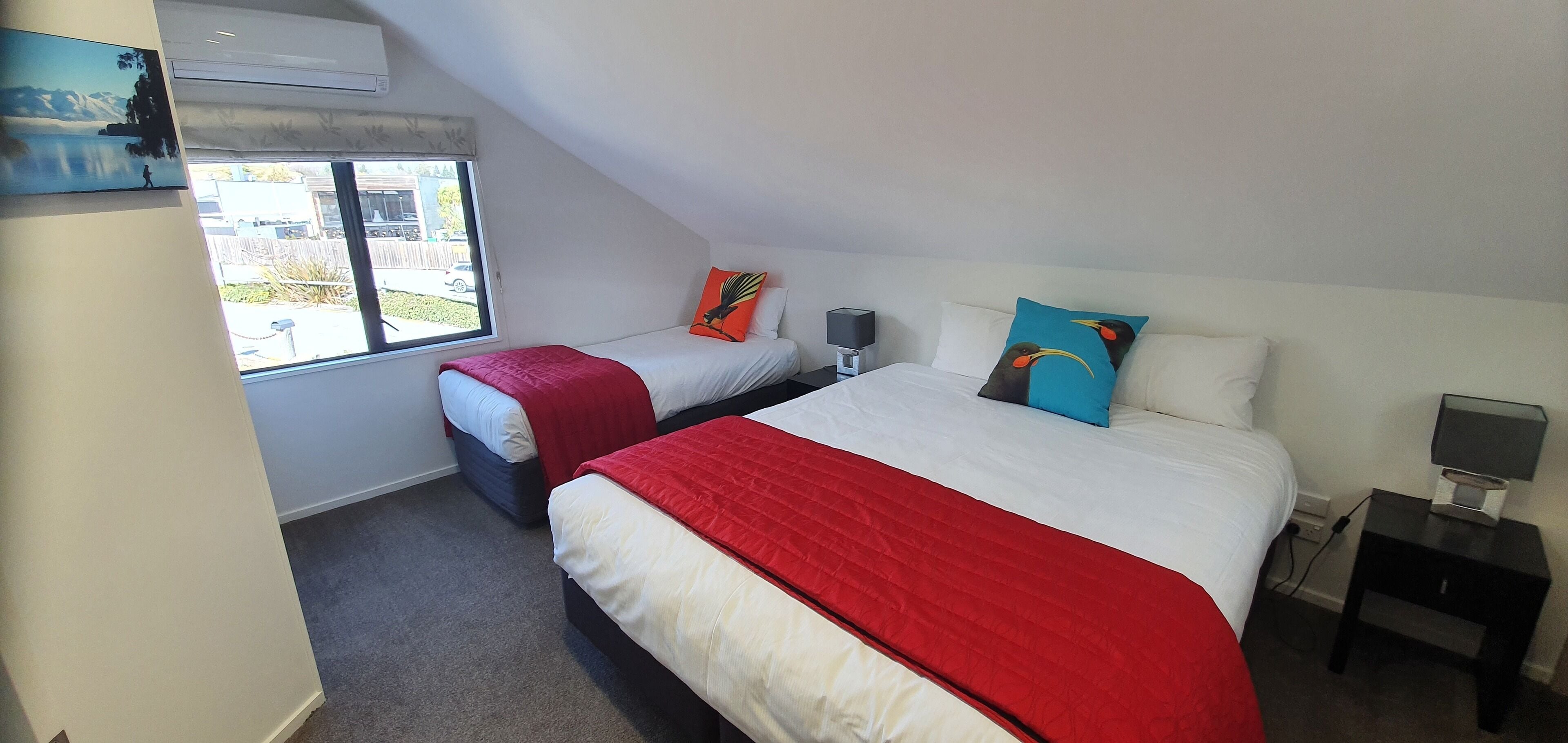 A bedroom with two beds, a window, a nightstand, and a wall-mounted air conditioner.