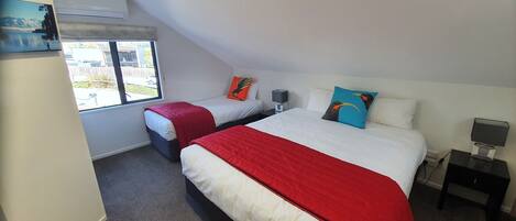 A bedroom with two beds, a window, a nightstand, and a wall-mounted air conditioner.