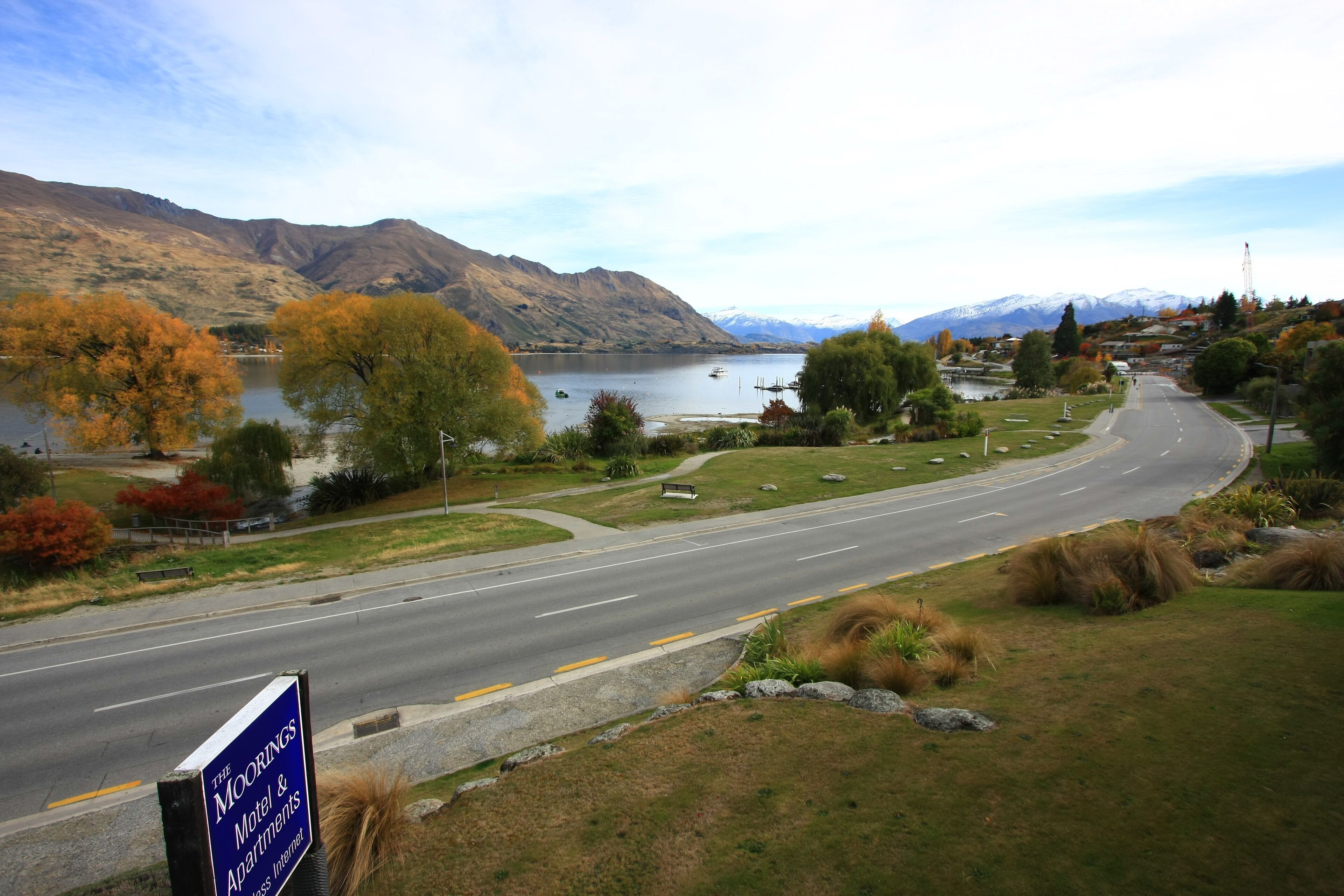 A road leading to The Moorings Motel & Apartments with a view of a lake and mountains in the background.