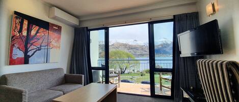 Habitación de hotel moderna con un amplio ventanal corredero que da a un balcón con vistas a una montaña y un lago.