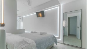 Un dormitorio moderno con cama, mesita de noche y televisor montado en la pared.
