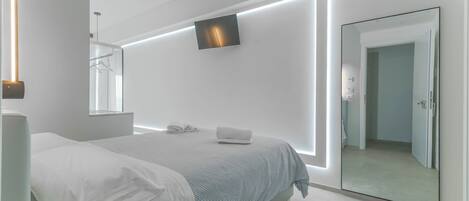 Un dormitorio moderno con cama, mesita de noche y televisor montado en la pared.