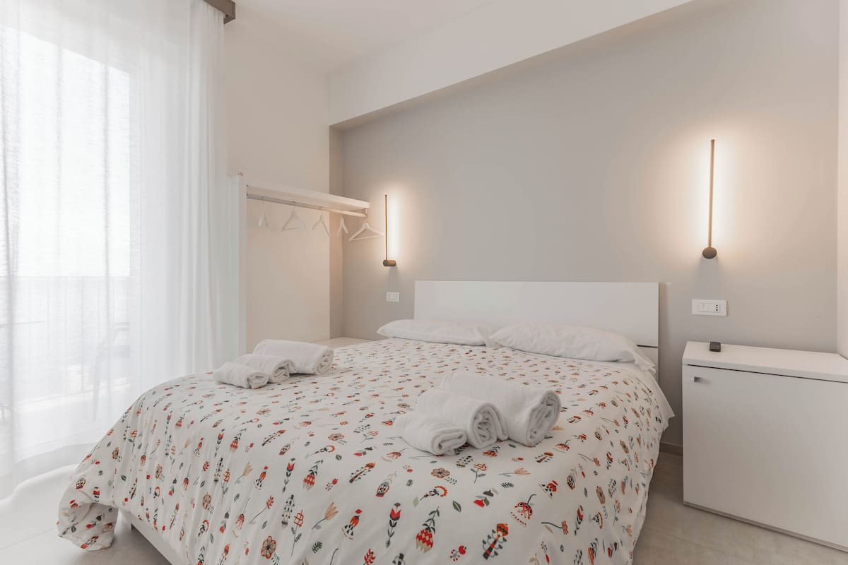 A neatly made bed with floral bedding, a bedside table, and two wall-mounted lights.