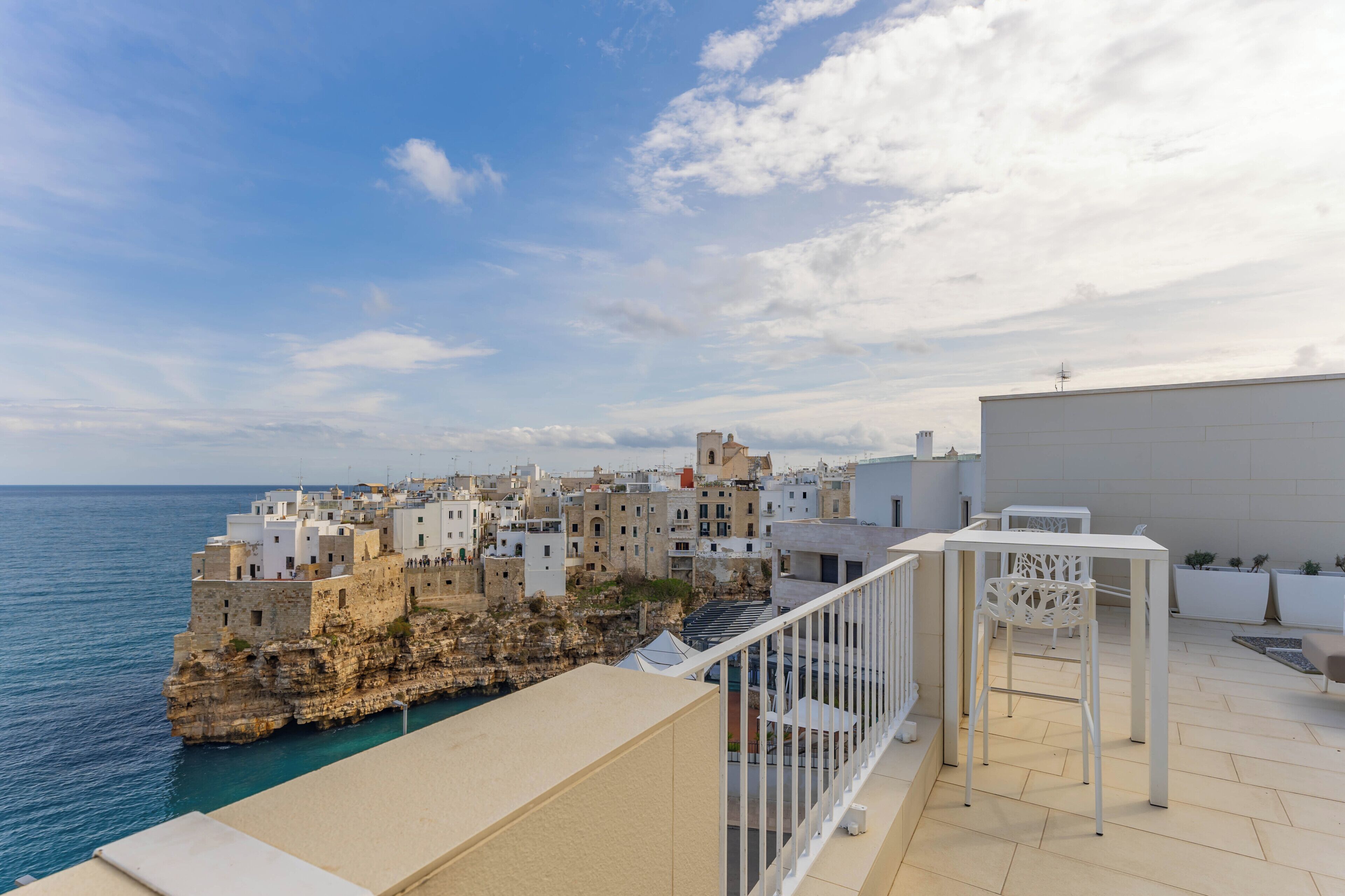 Une ville côtière avec des bâtiments construits le long de la falaise, un balcon avec une table et des chaises, et une vue sur la mer.