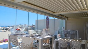 Terraza en la azotea con mobiliario blanco, una mesa con un cuenco y vistas a la ciudad.