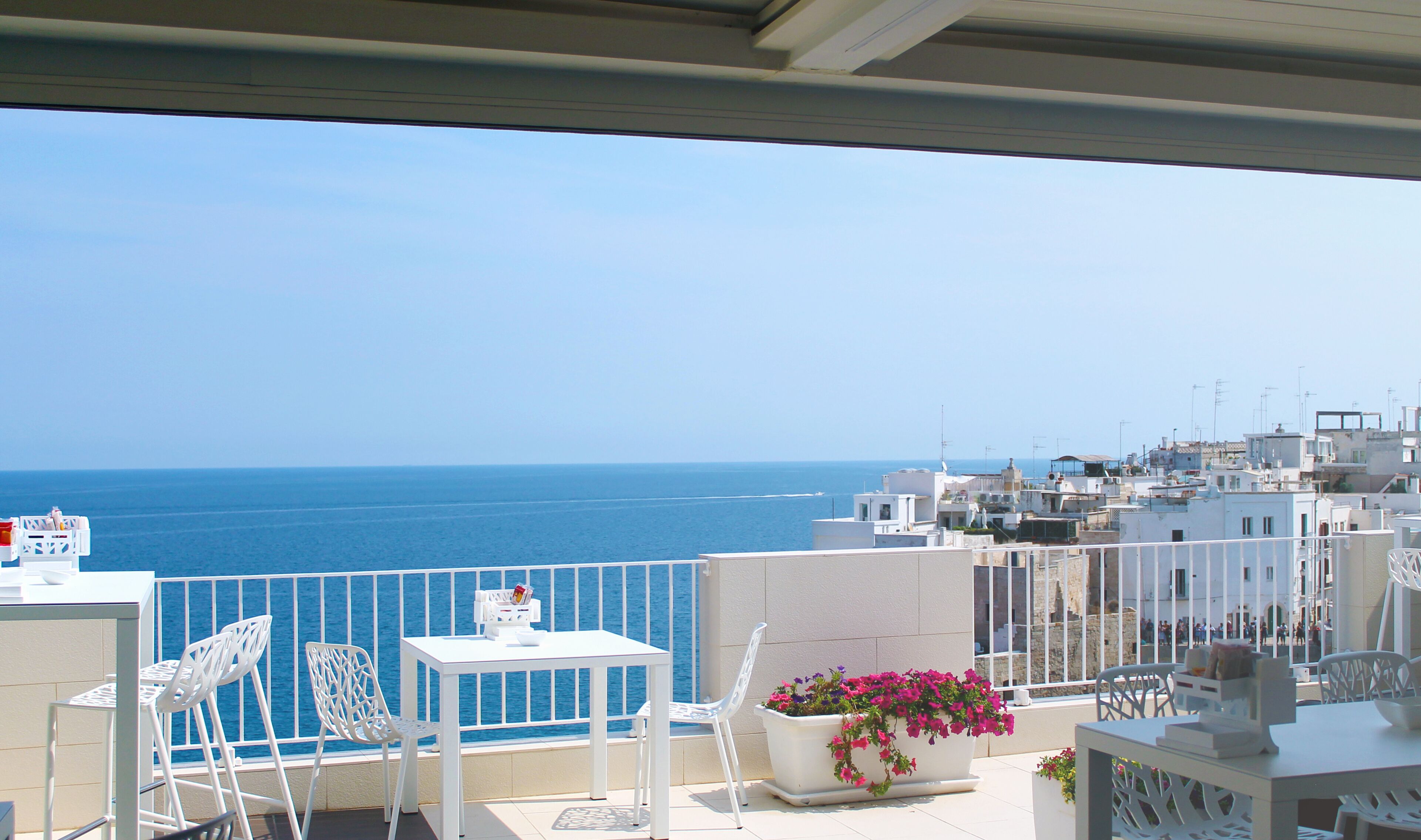 Un balcon avec vue sur la mer, des meubles blancs et un pot de fleurs.
