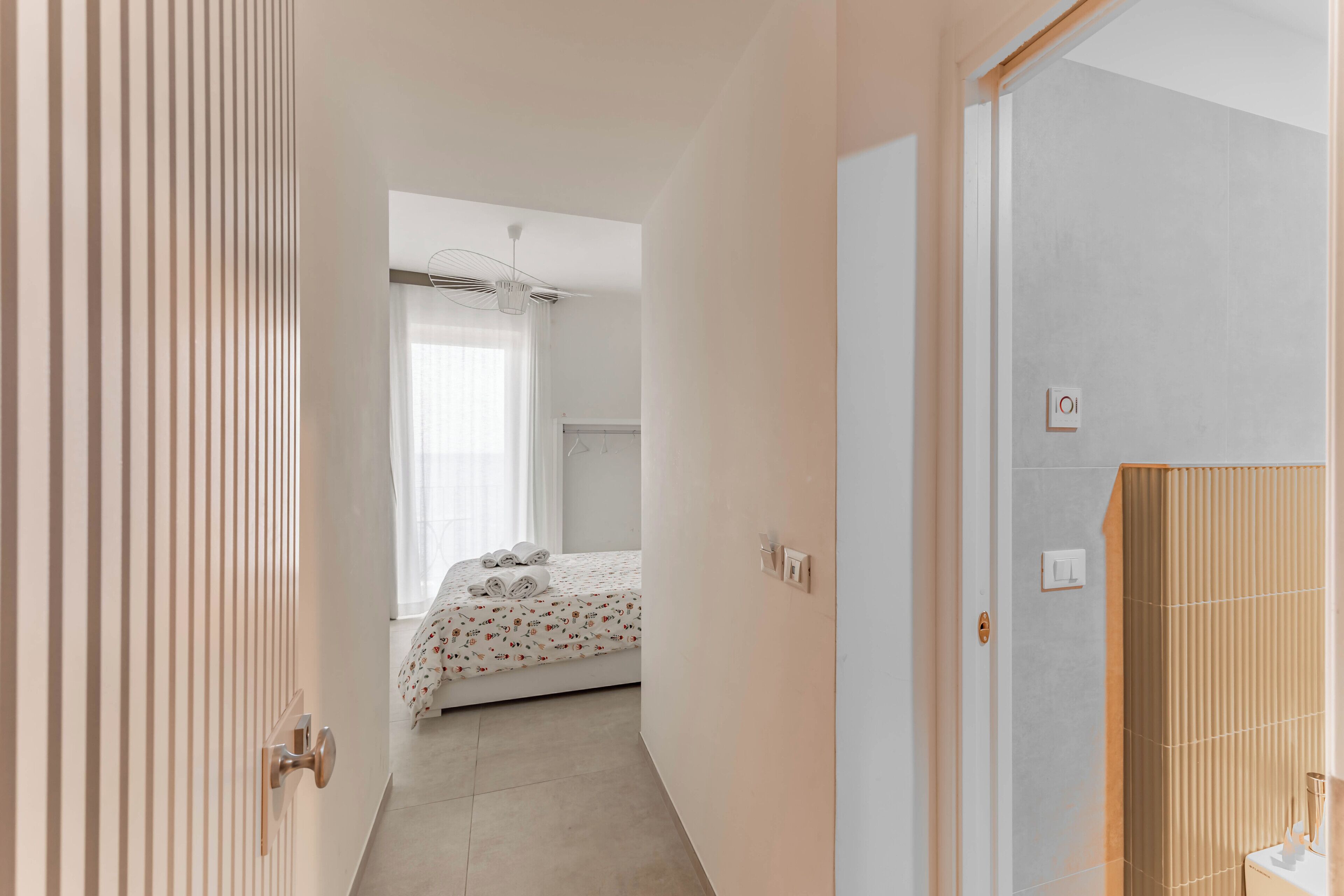 Una habitación de hotel con cama, ventana con cortinas, puerta y baño con perchero.