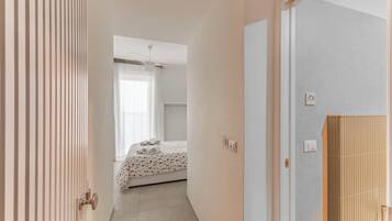 Una habitación de hotel con cama, ventana con cortinas, puerta y baño con perchero.