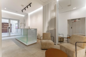 A modern hotel lobby with a reception desk, seating area, and an elevator. - Dimore del Malù (Polignano a Mare)