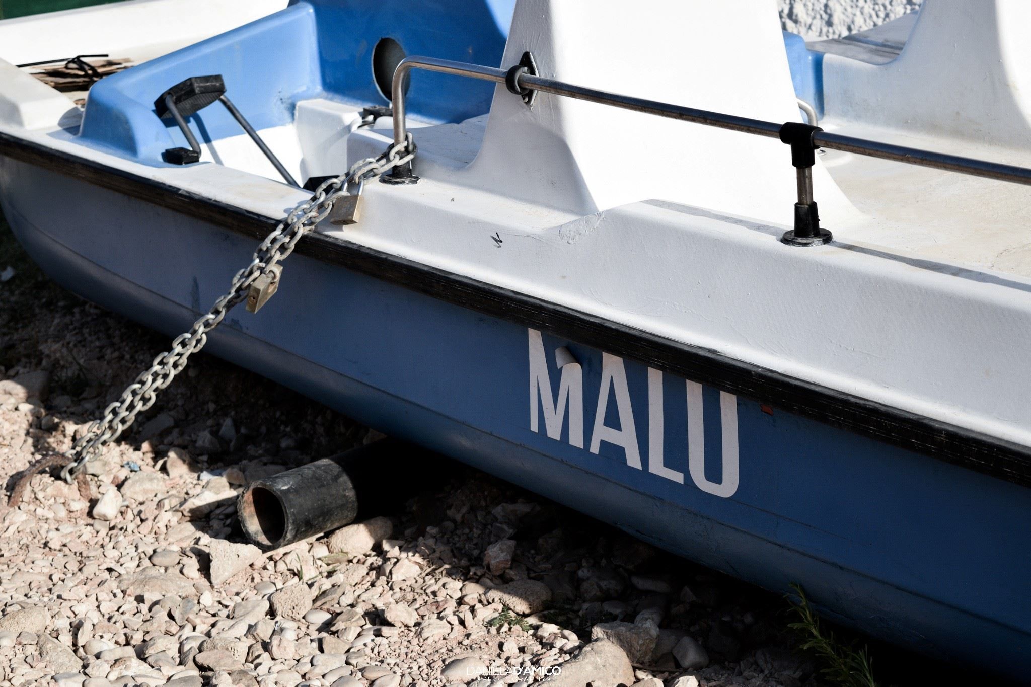 A boat with the name "MALU" on its side, tied to a dock with a chain.