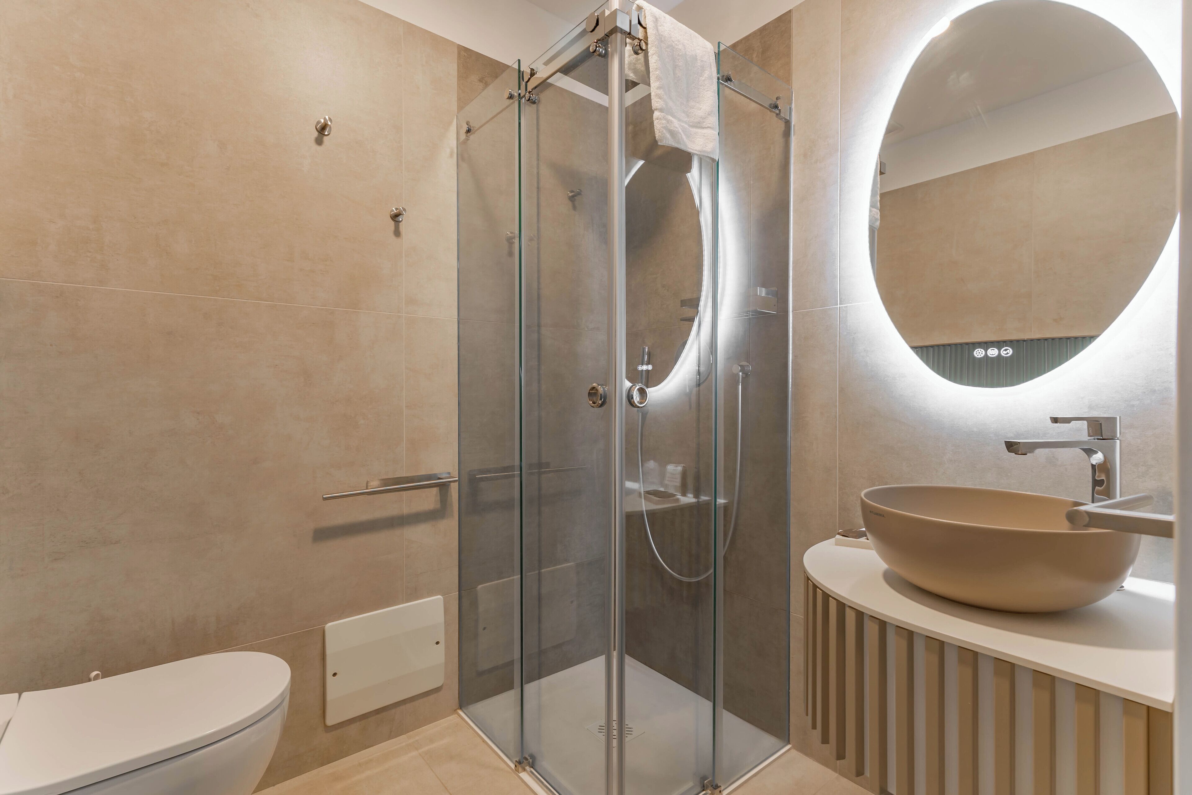 Un baño moderno con ducha envuelta en vidrio, un espejo redondo y un lavabo sobre encimera.
