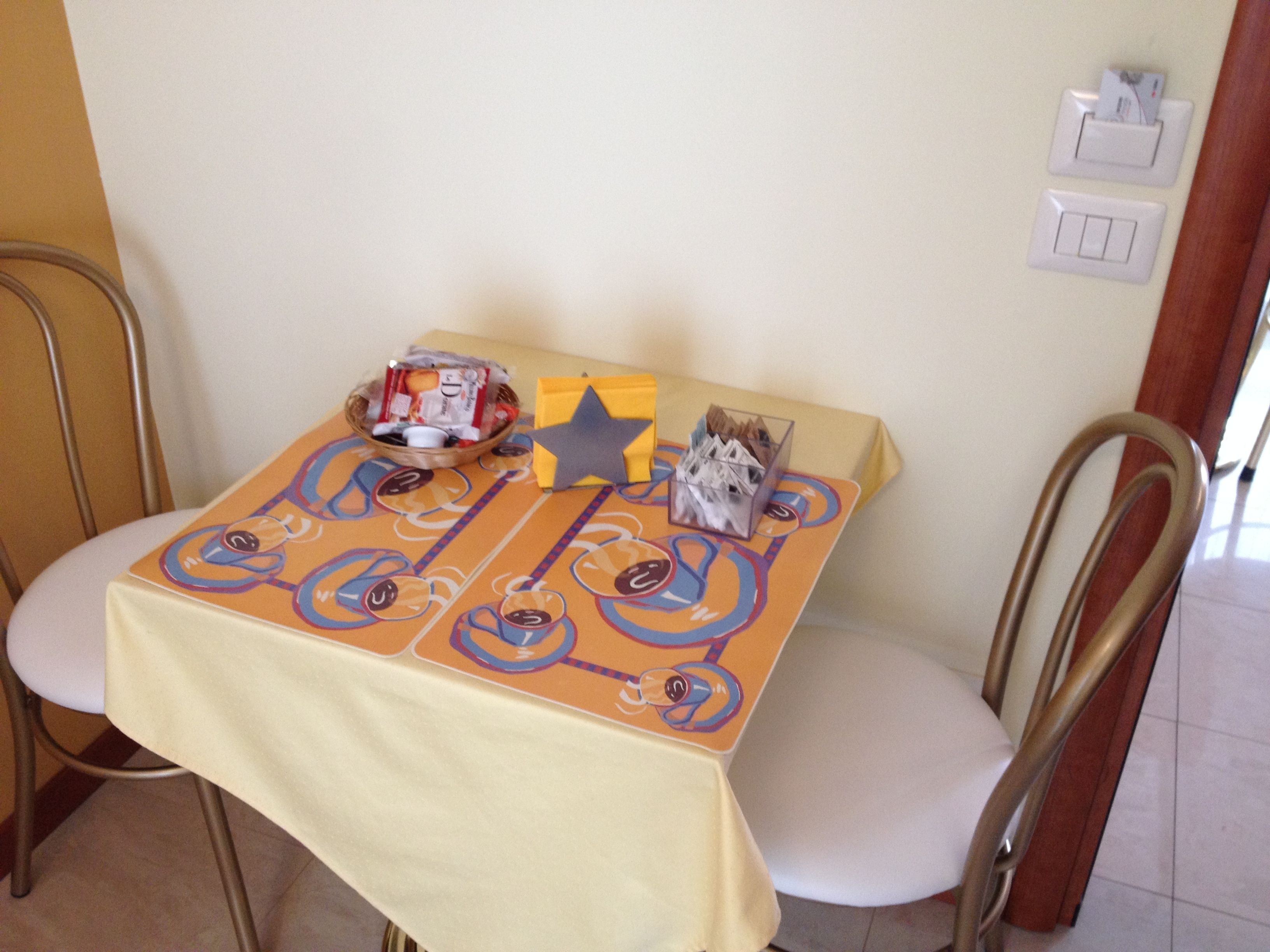 A dining table with a yellow tablecloth, two chairs, a basket of snacks, a star-shaped napkin holder, and a small box of tissues.