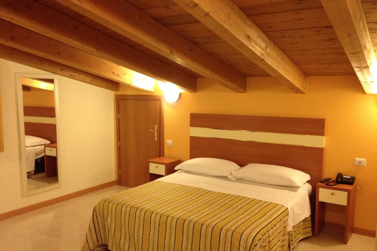 Ein Schlafzimmer mit Holzboden, einem Bett mit gestreifter Bettdecke, einem Nachttisch mit Lampe und einem Beistelltischchen mit Telefon.
