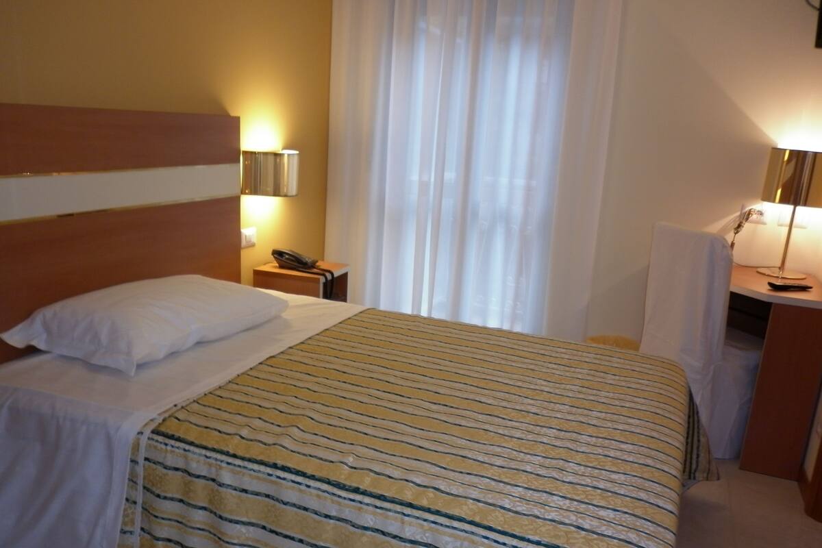 Ein Hotelzimmer mit einem Bett, einem Nachttisch mit Lampe, einem Telefon und einem Sessel.