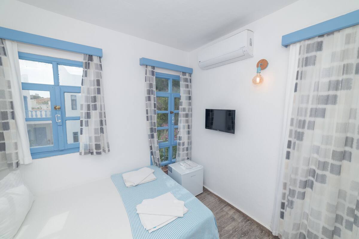 A bedroom with a bed, a bedside table, a TV, and a window with curtains.