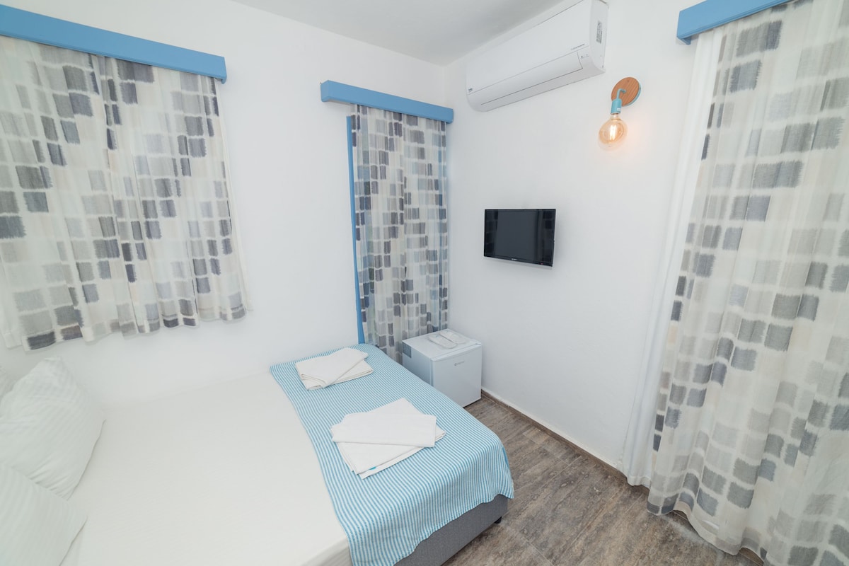 A bedroom with a bed, a bedside table, a TV, and a window with curtains.