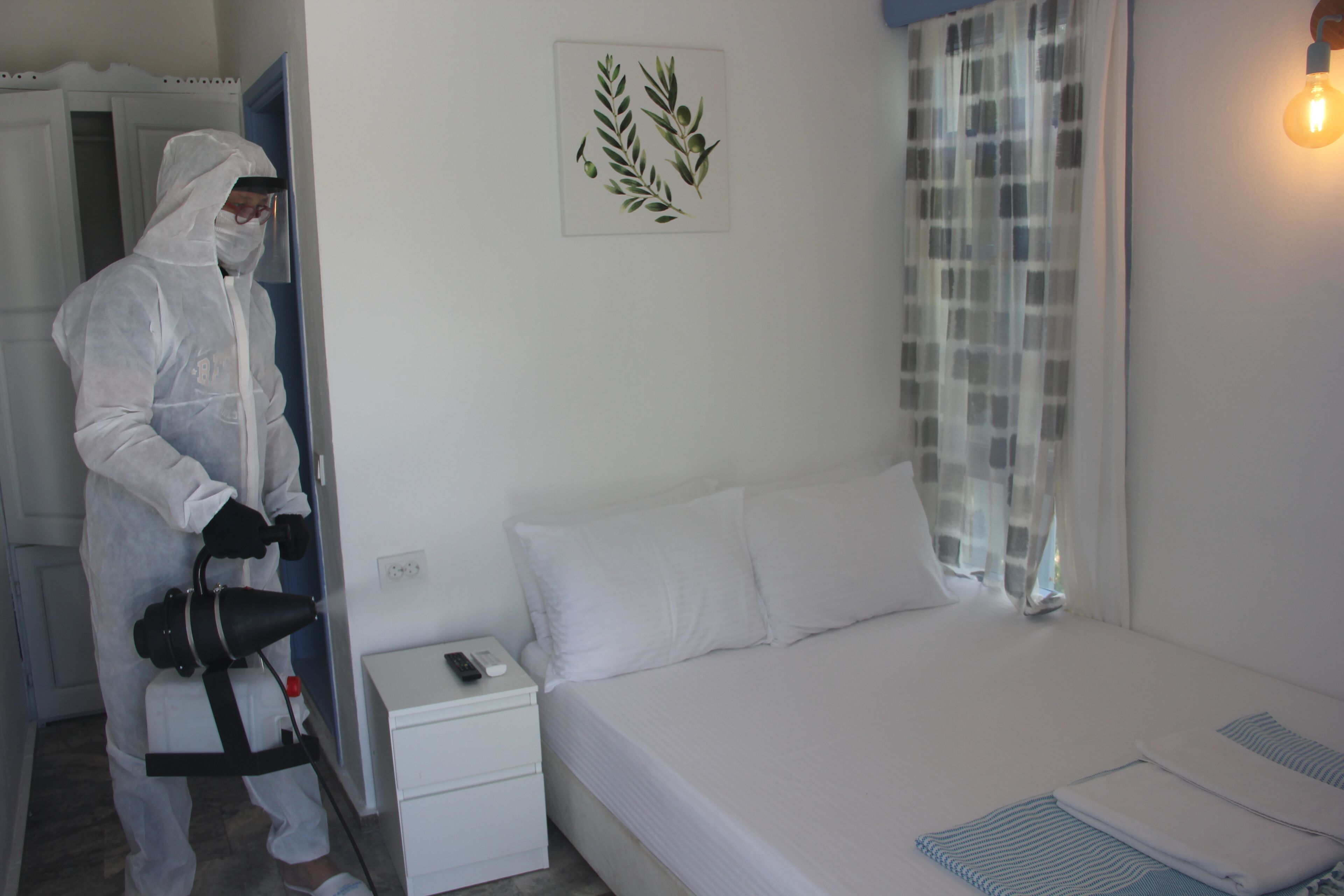 A hotel room with a bed, a nightstand, a remote control, and a wall-mounted light fixture.