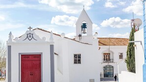 A white church with a red door, a bell tower, and a small bell. - Casa Do Platano (Arraiolos)