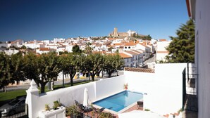 A residential area with a swimming pool, trees, and a distant castle-like structure. - Casa Do Platano (Arraiolos)