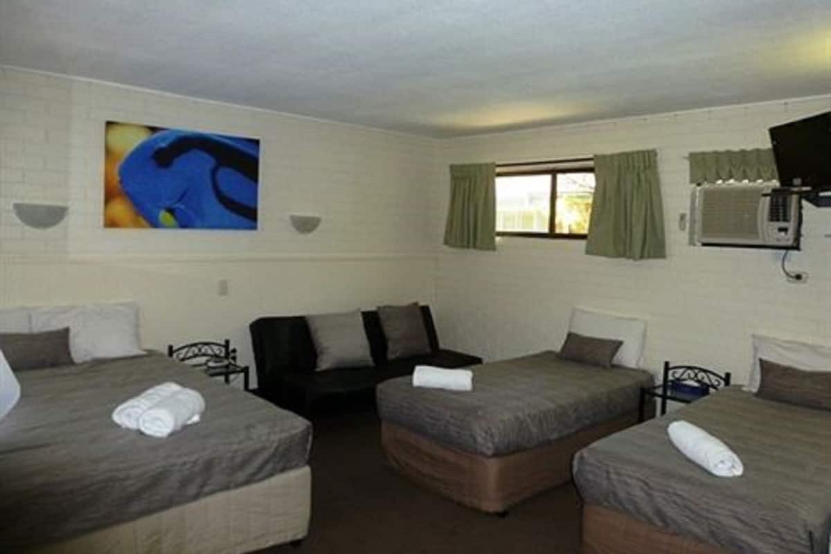 A hotel room with two single beds, a sofa, a small table, and a window with curtains.