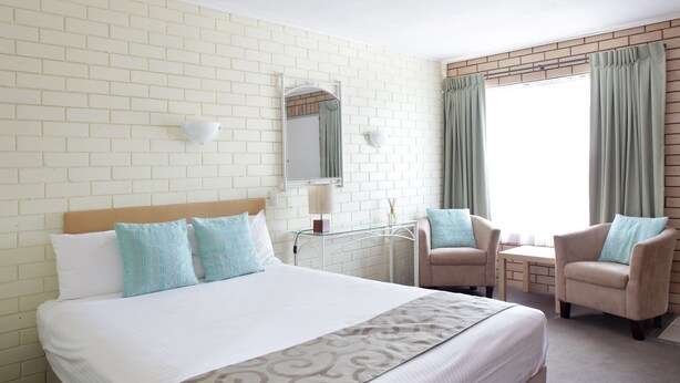 Habitación de hotel con una cama grande, dos sillones, una mesita, un espejo y una ventana con cortinas.