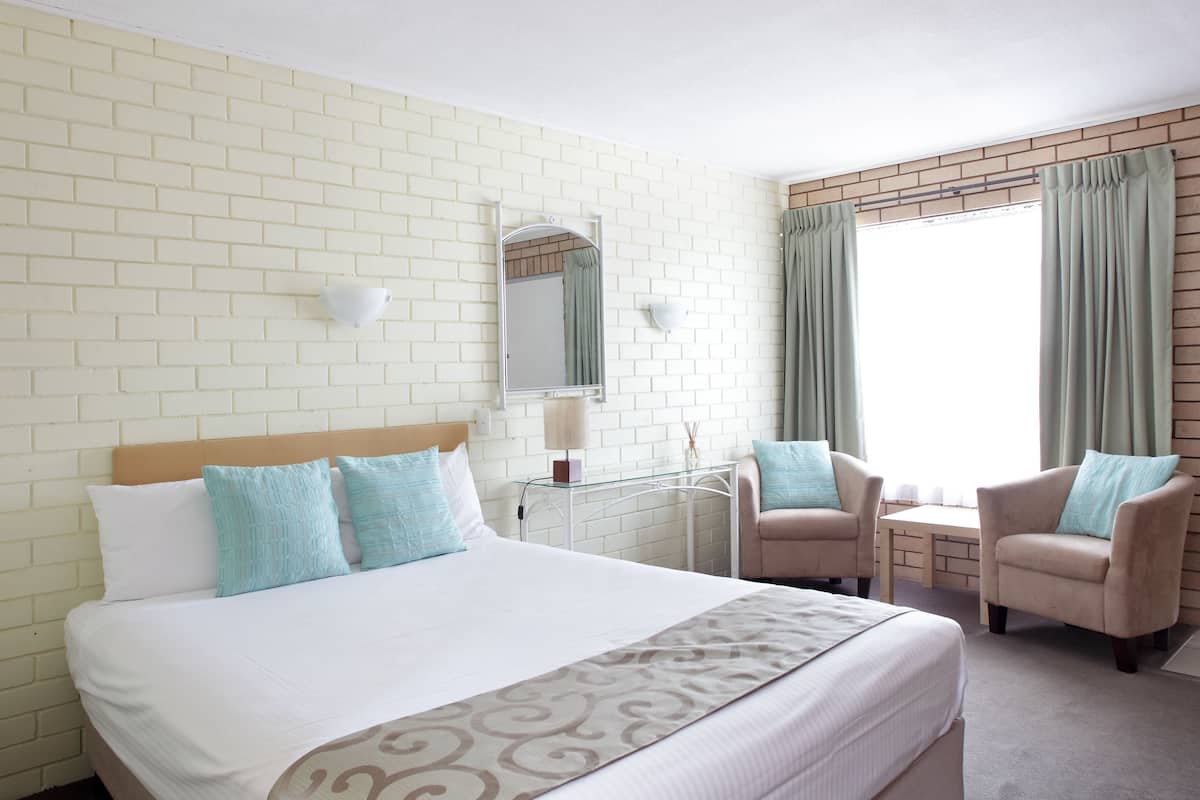 A hotel room with a large bed, two armchairs, a small table, a mirror, and a window with curtains.