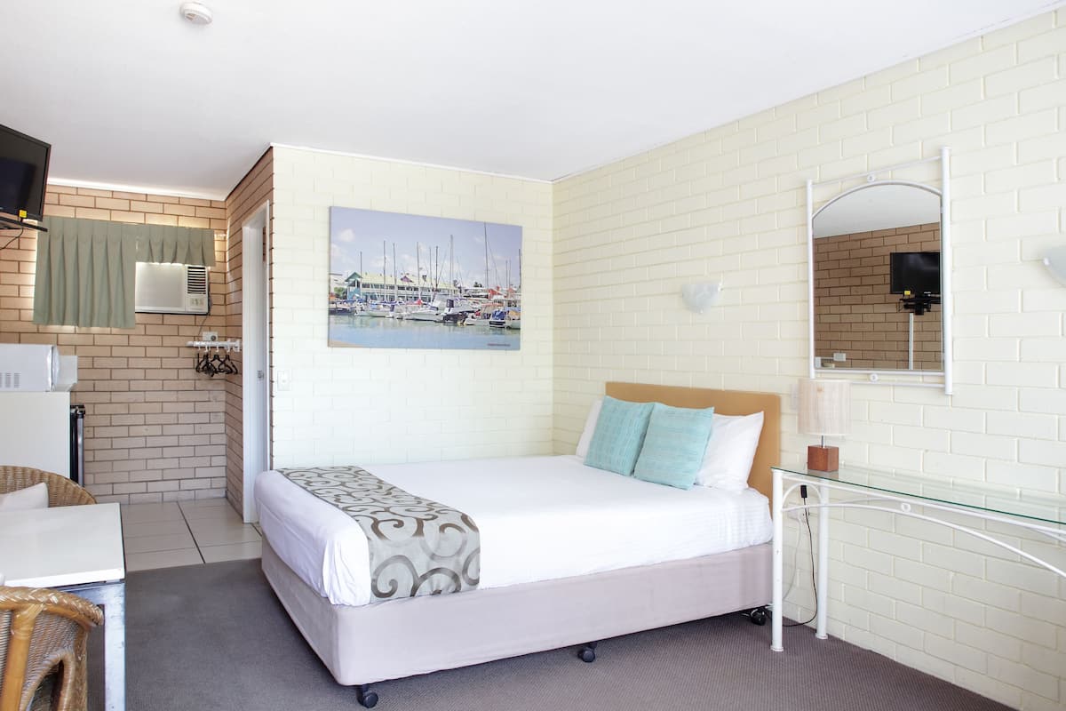 A hotel room with a bed, a desk, a chair, a TV, and a painting of a marina.