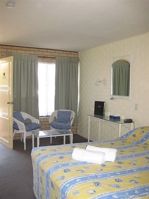 A hotel room with a bed, two chairs, a small table, a desk with a computer, and a window with curtains. - Twin Pines Motel (Mooloolaba)