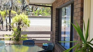 Un patio al aire libre con una mesa redonda y sillas, rodeado de paredes de ladrillo y ventanas grandes.