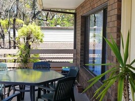 Un patio al aire libre con una mesa redonda y sillas, rodeado de paredes de ladrillo y ventanas grandes.