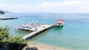 A pier with lounge chairs and umbrellas, a boat docked at the end, and clear blue water. - Comfy Hostel Studios (Corfu)