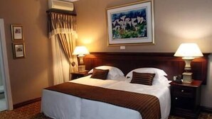 Une chambre d’hôtel avec un grand lit, deux tables de chevet avec des lampes, un tableau au mur et une moquette à motifs.