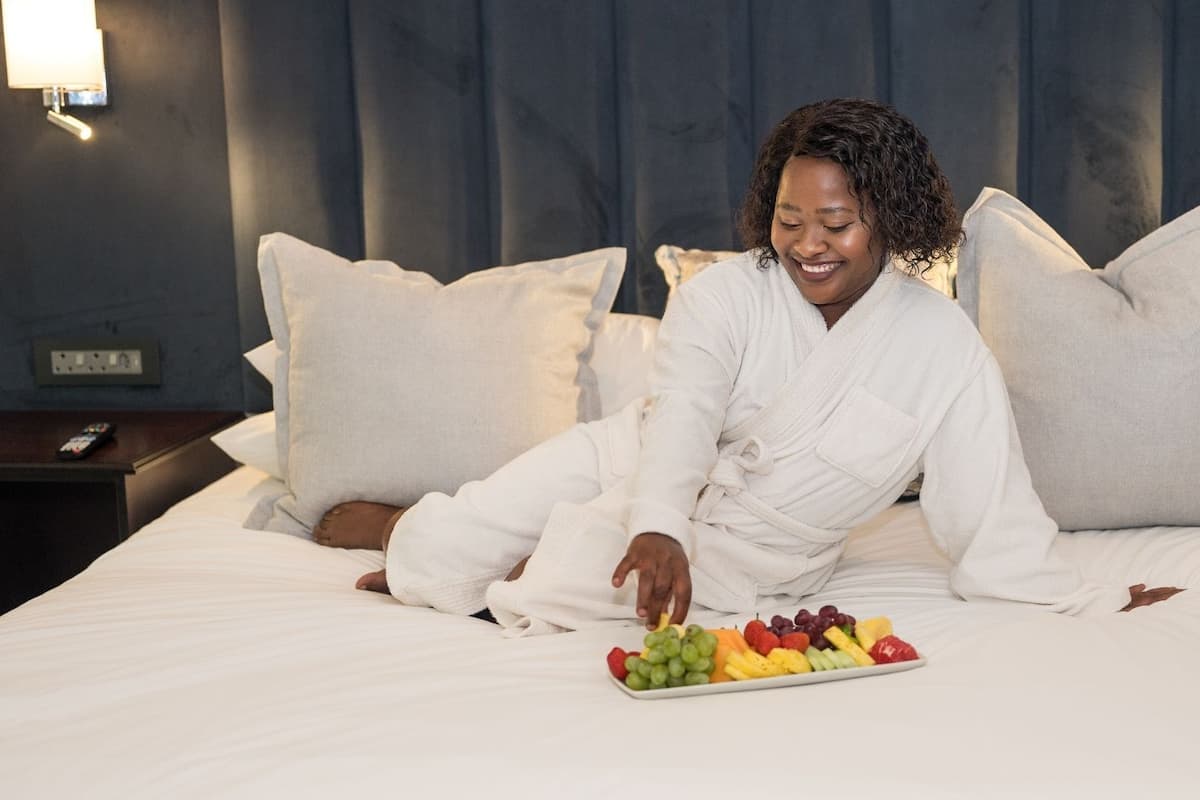A person sitting on a bed with a tray of fruit in front of them.