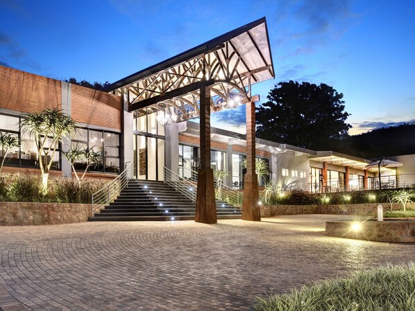 Un edificio moderno con fachada de vidrio, una escalera que conduce a la entrada y zonas de estar al aire libre.