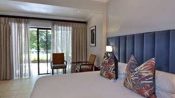 A hotel room with a large bed, two chairs, a table, and a view of the outdoors through a sliding door.
