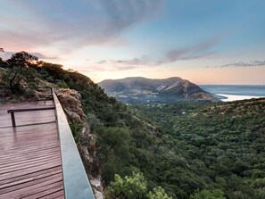 Una terraza de madera con vistas a un paisaje montañoso, un bosque denso y una masa de agua.