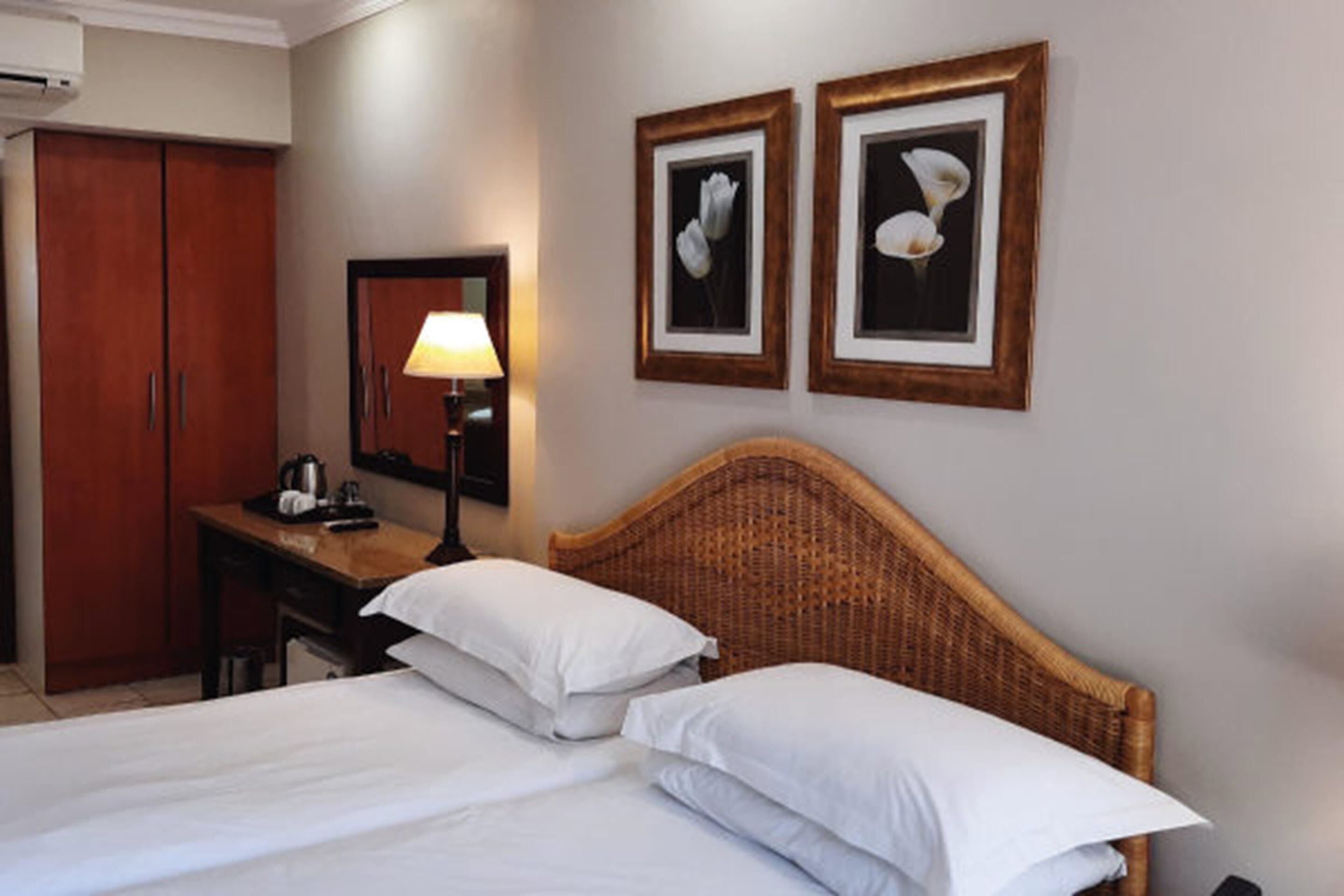 Een hotelkamer met een bed, een bureau, een lamp en twee ingelijste foto’s aan de muur.
