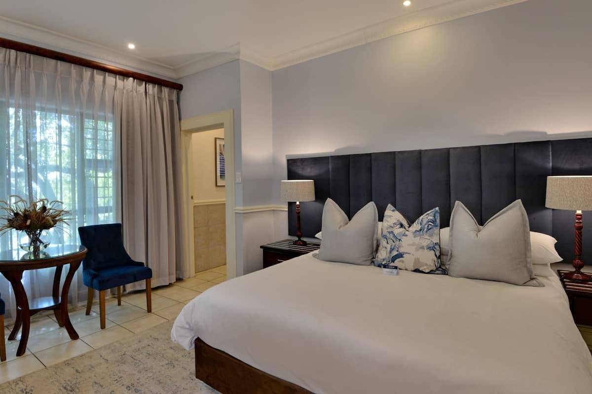 A hotel room with a large bed, two bedside tables, a chair, a small table with a vase, and a window with curtains.